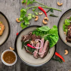 Trzy talerze z mięsem, jedno danie przypomina carpaccio z wołowiny, ozdobione ziołami, orzechami i papryczkami chili.