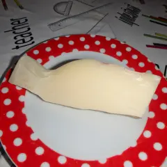 Kawałek żółtego sera provolone leży na talerzu w czerwone kropki. Tło przedstawia materiał z rysunkami przyborów szkolnych.