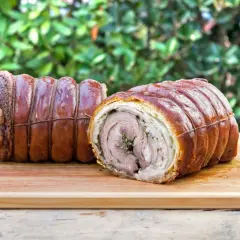 Dwa pieczone kawałki porchetta, zawinięte w skórkę i sznurki, leżą na desce. To pyszne danie, które warto poznać!