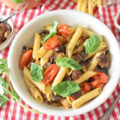 Penne z bakłażanem, pomidorkami i oliwkami, ozdobione bazylią. Smaki kuchni sycylijskiej na talerzu.
