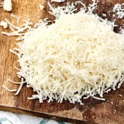Strugane parmigiano reggiano na drewnianej desce, idealne do posypania makaronu, risotto lub zapiekanek.