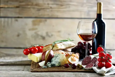 Degustacja najpopularniejszych win włoskich: kieliszek wina, butelka, sery, wędliny, pieczywo, winogrona i pomidorki.