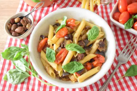 Penne z bakłażanem, pomidorkami i oliwkami, ozdobione bazylią. Smaki kuchni sycylijskiej na talerzu.