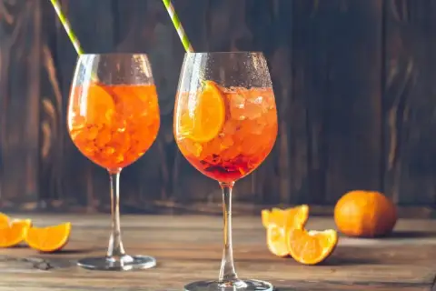 Dwa orzeźwiające drinki Aperol z pomarańczą i słomkami, na drewnianym stole.