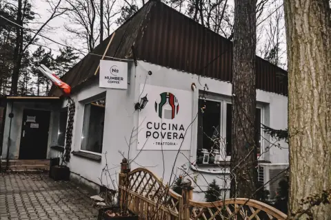 Biały budynek z logo "Cucina Povera - Trattoria" i szyldem "Number Coffee" w otoczeniu drzew.