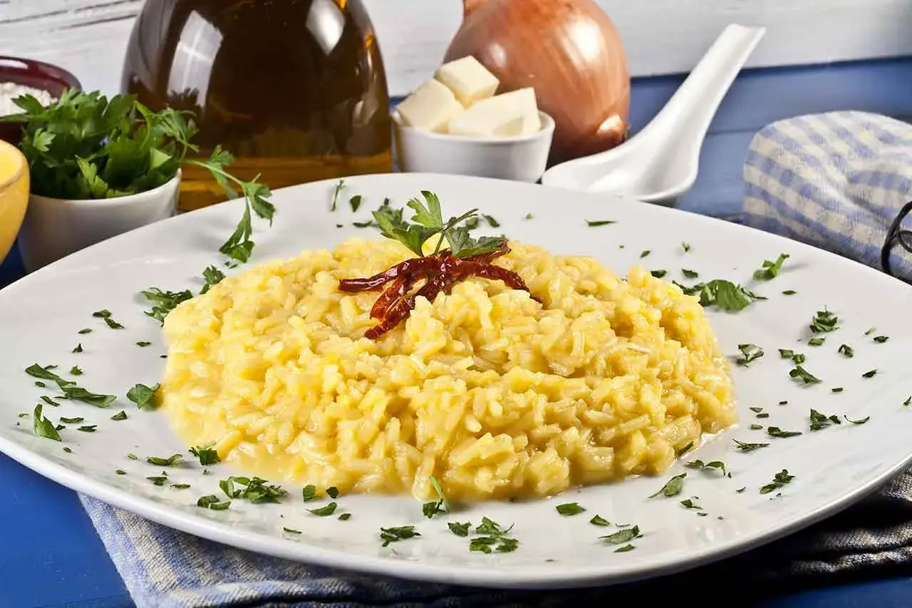 Pyszne risotto alla milanese, kremowe i aromatyczne, ozdobione suszonymi papryczkami i natką pietruszki.