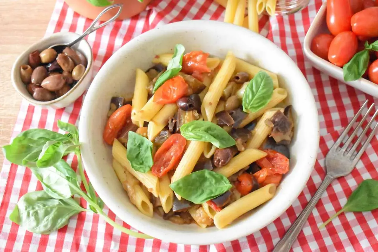 Penne z bakłażanem, pomidorkami i oliwkami, ozdobione bazylią. Smaki kuchni sycylijskiej na talerzu.