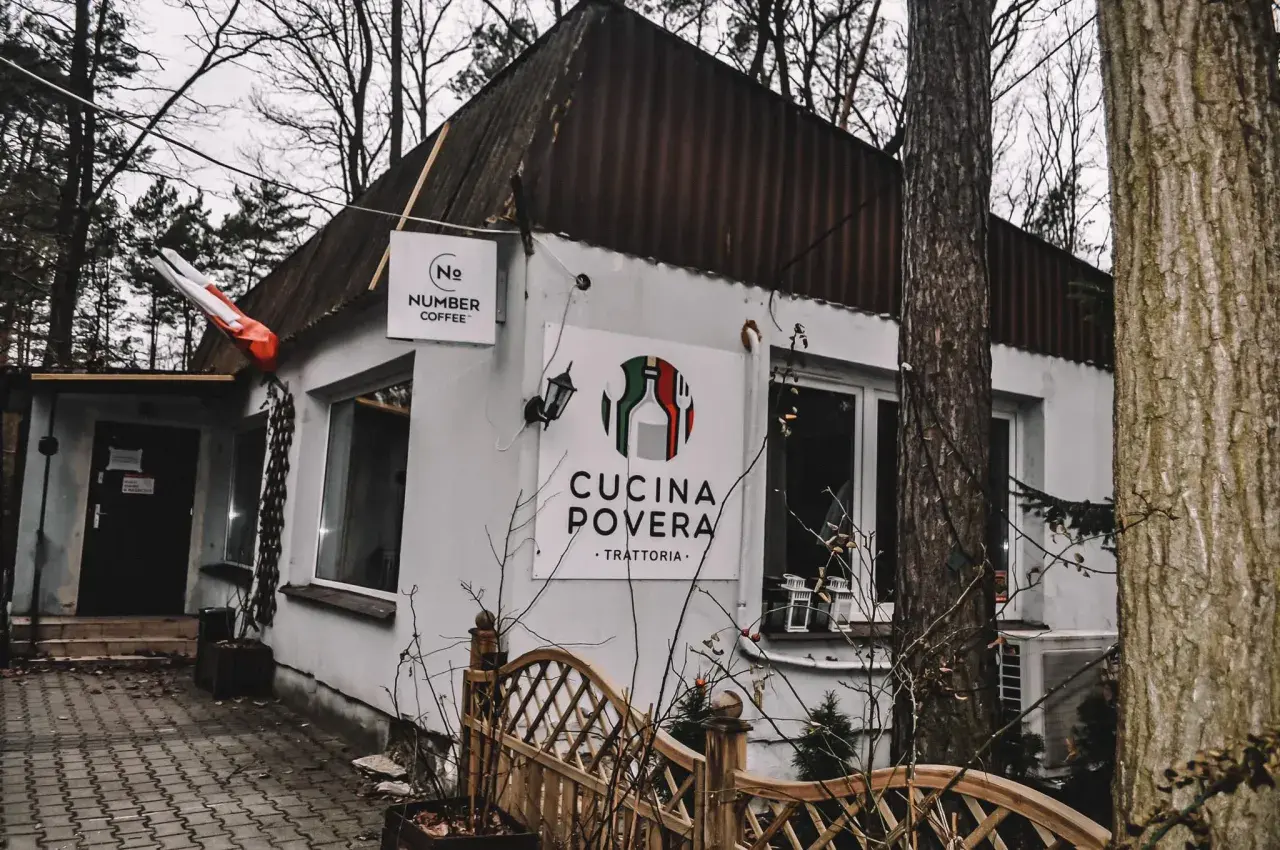 Biały budynek z logo "Cucina Povera - Trattoria" i szyldem "Number Coffee" w otoczeniu drzew.