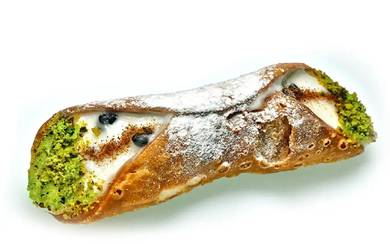 Sycylijska kuchnia w pysznej odsłonie: cannolo z kremem, pistacjami i borówkami, posypane cukrem pudrem.