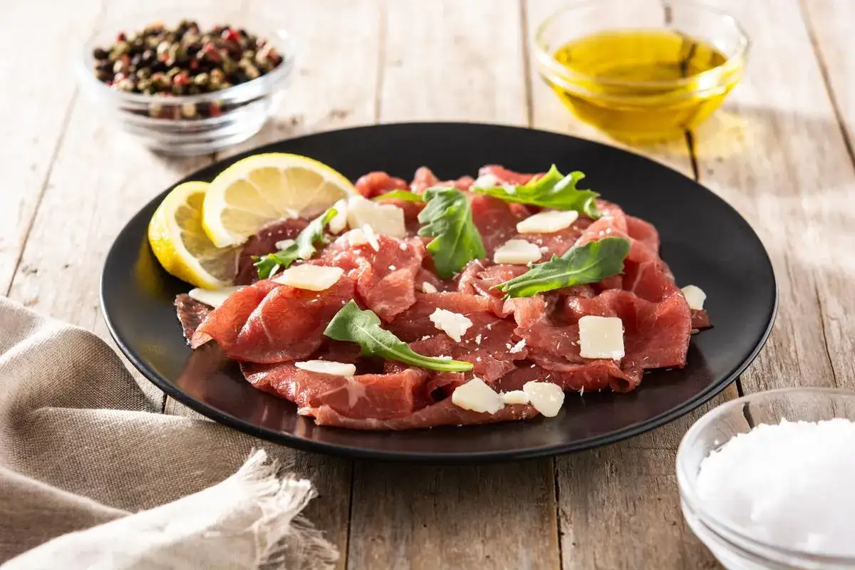 Eleganckie carpaccio wołowe z rukolą i parmezanem, podane z cytryną i oliwą. Idealne na lekki posiłek.