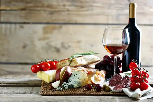 Degustacja najpopularniejszych win włoskich: kieliszek wina, butelka, sery, wędliny, pieczywo, winogrona i pomidorki.