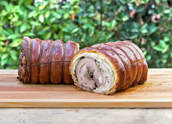 Dwa pieczone kawałki porchetta, zawinięte w skórkę i sznurki, leżą na desce. To pyszne danie, które warto poznać!